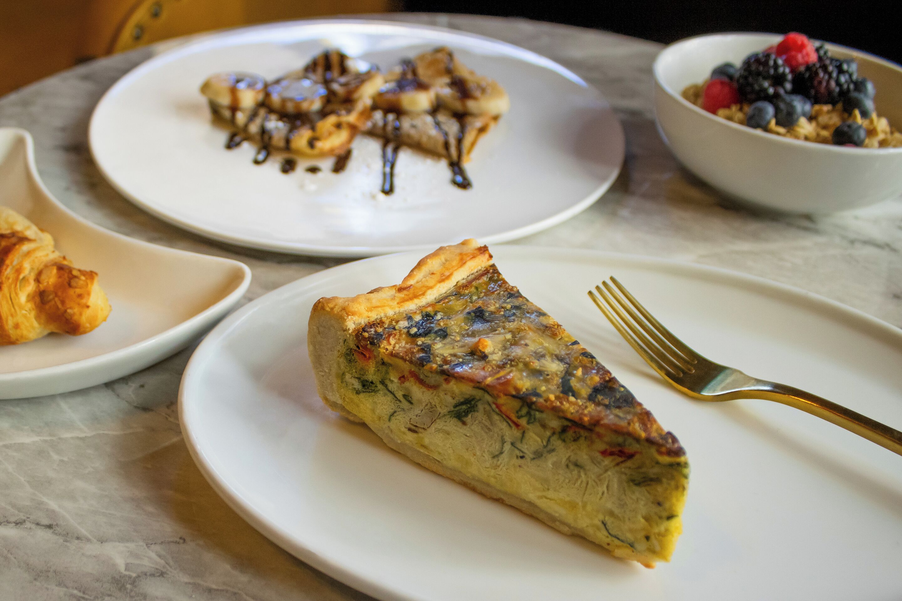 A table with plates of food, including a slice of quiche and a bowl of berries.