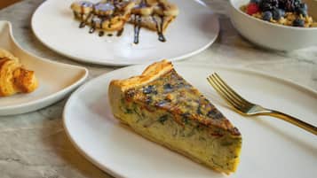 A table with plates of food, including a slice of quiche and a bowl of berries.