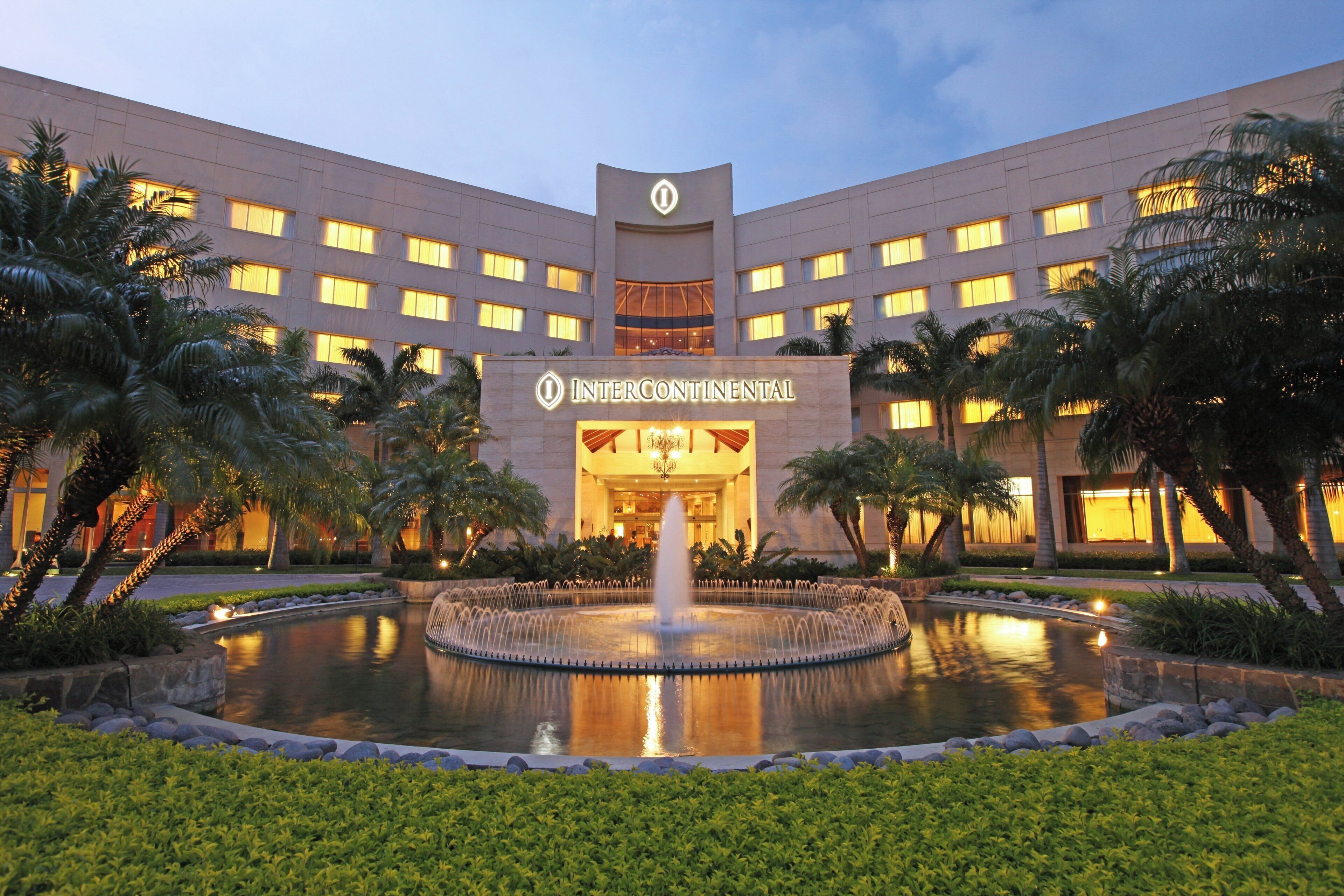 Un hotel con una fuente central, rodeado de palmeras y exuberante vegetación.