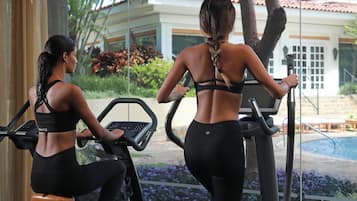Two individuals using stationary bikes in a gym with a view of a building and trees outside.