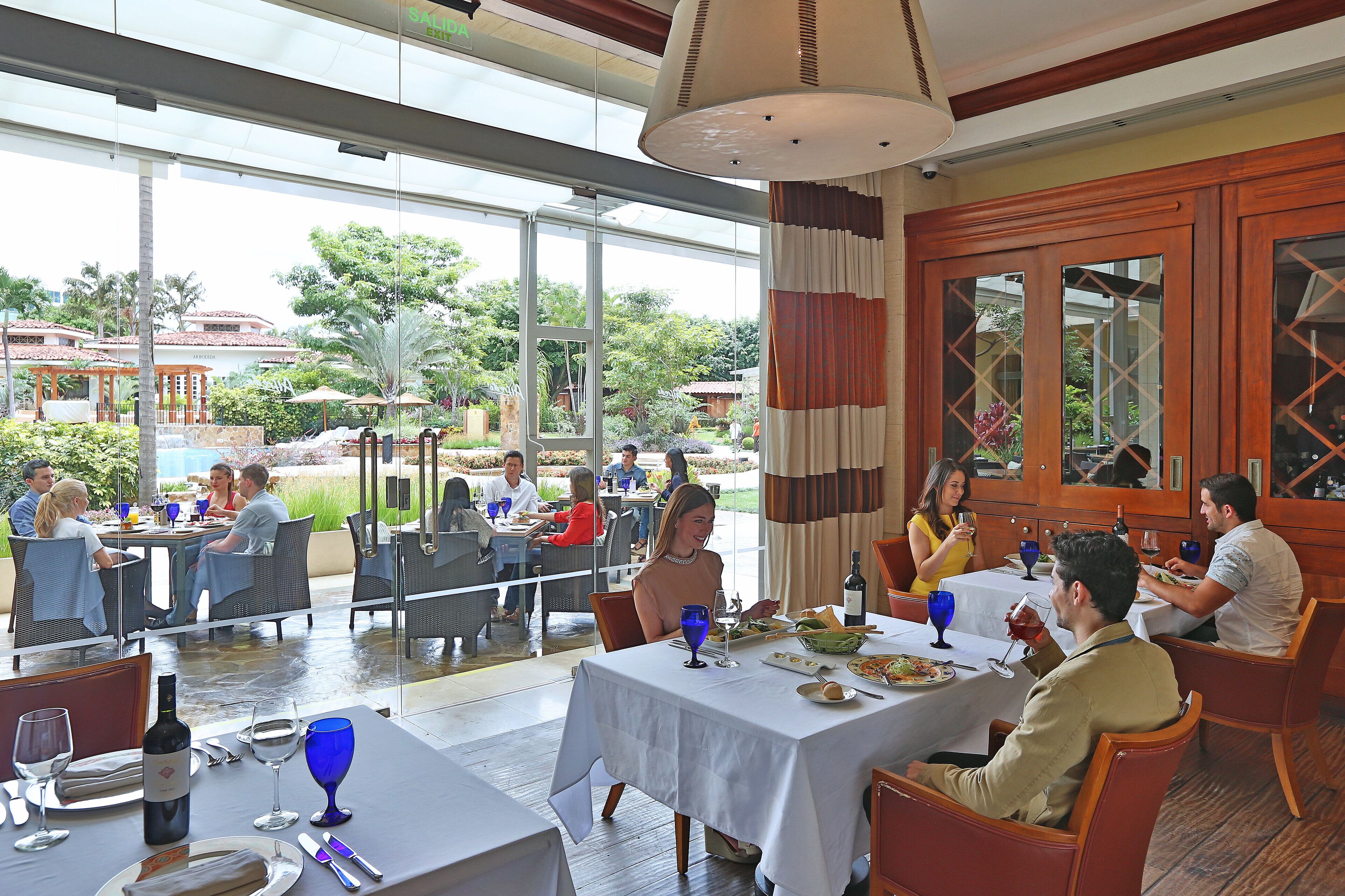 A restaurant with outdoor seating, large windows, and a view of the garden.