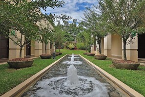 A courtyard with a central water feature, surrounded by trees and planters, and buildings with beige walls and columns. - InterContinental Costa Rica at Multiplaza Mall by IHG (San Rafael)
