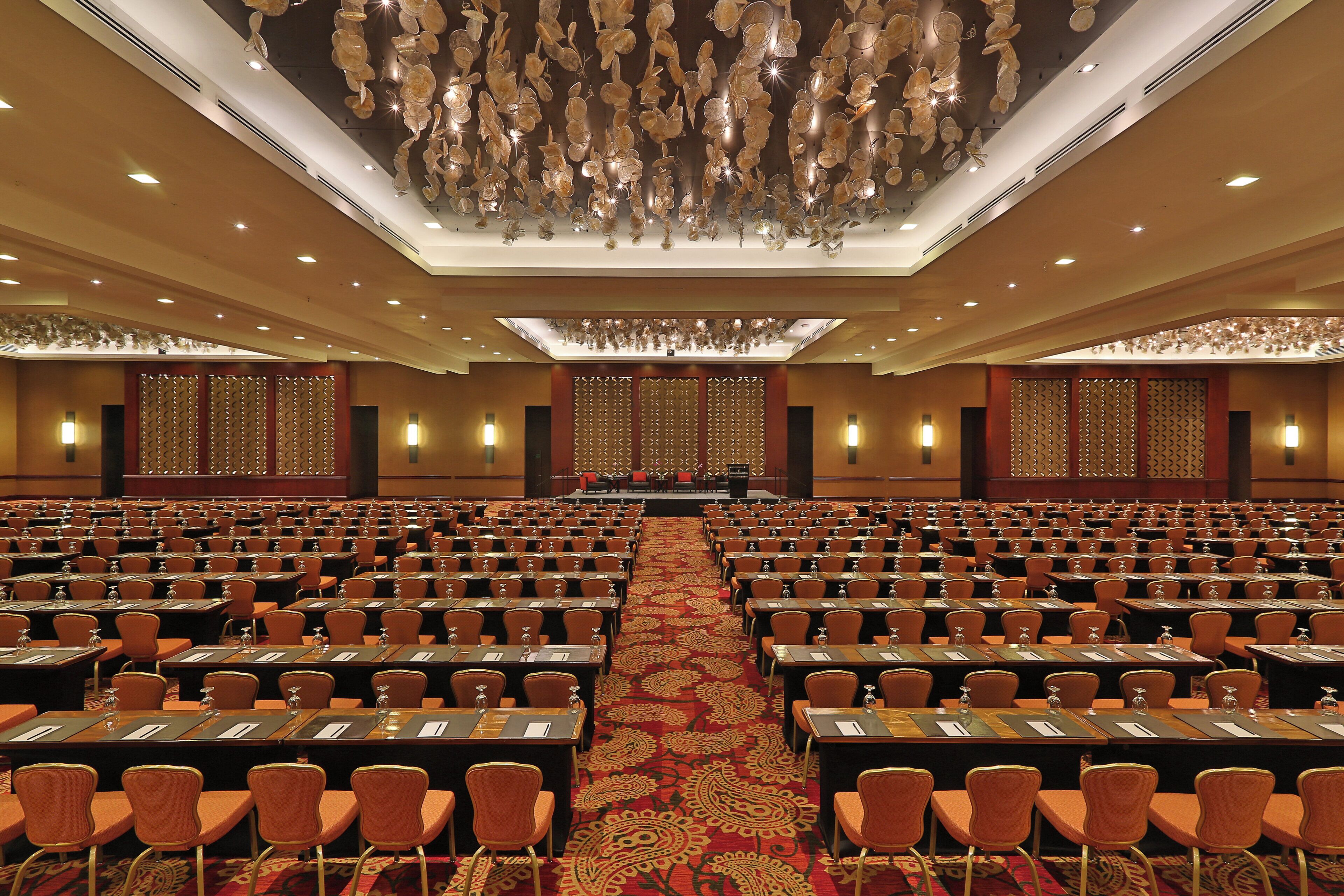 A large conference room with rows of tables and chairs, a patterned carpet, and a decorative ceiling.