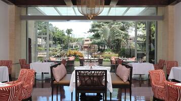 A restaurant with tables and chairs, a large window, and a view of a garden.