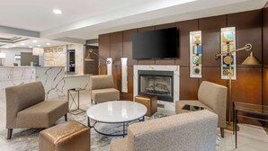 A modern living room with a fireplace, comfortable seating, a flat-screen TV, and a reception desk.