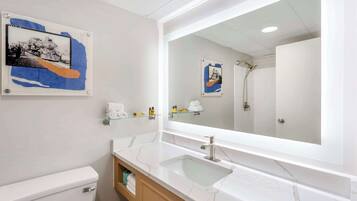 Un baño con inodoro blanco, lavamanos de vidrio, un espejo grande y dos cuadros en la pared.