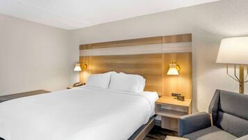 A hotel room with a large bed, two bedside tables with lamps, a chair, and a nightstand with a clock.