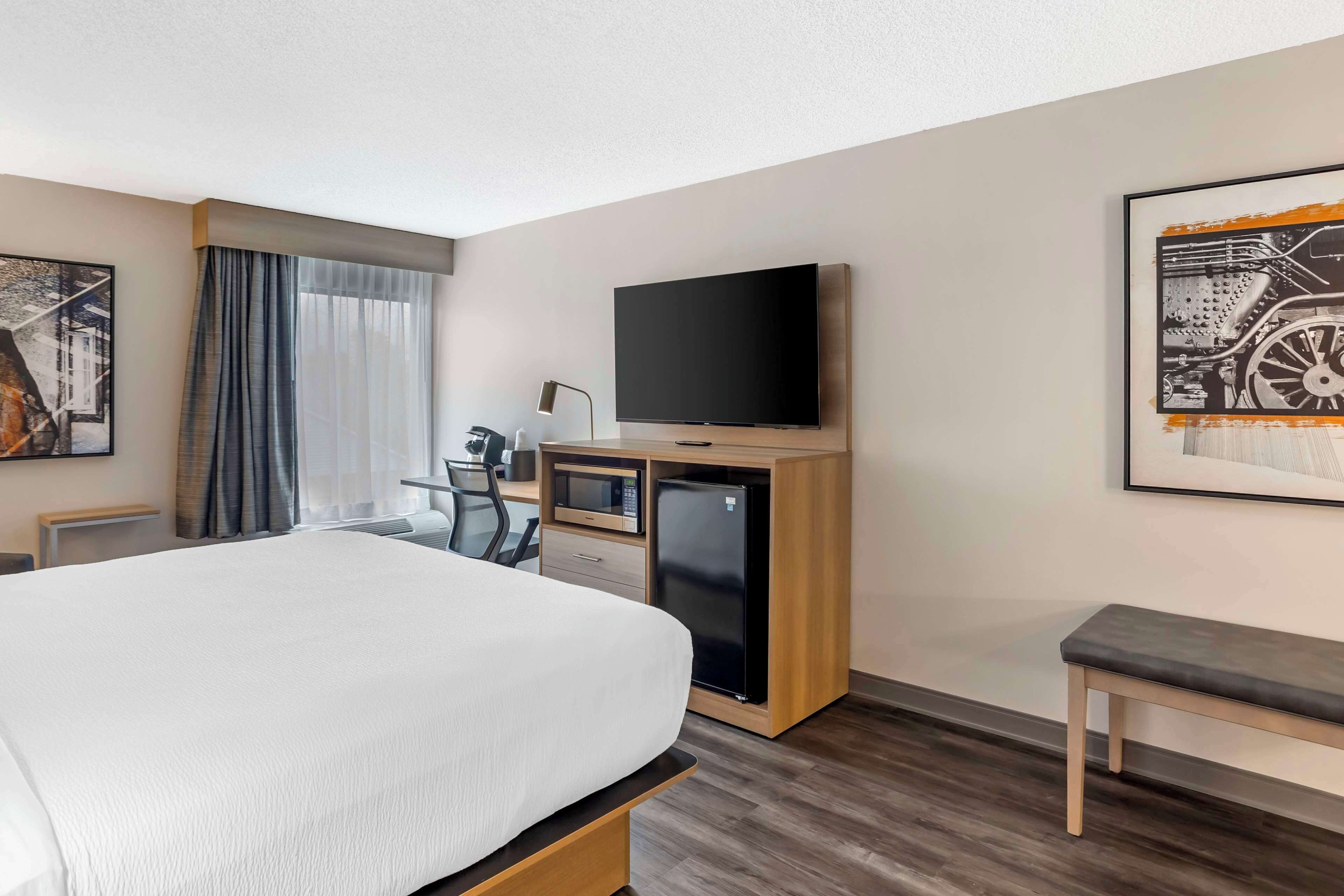 Een hotelkamer met een groot bed, een bureau met een computer, een televisie en een koelkast.