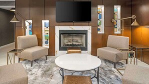 A modern living room with a fireplace, two armchairs, a round table, and a flat-screen TV mounted above the fireplace.