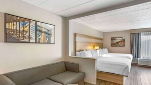 A hotel room with a bed, a sofa, a small table, and artwork on the walls.