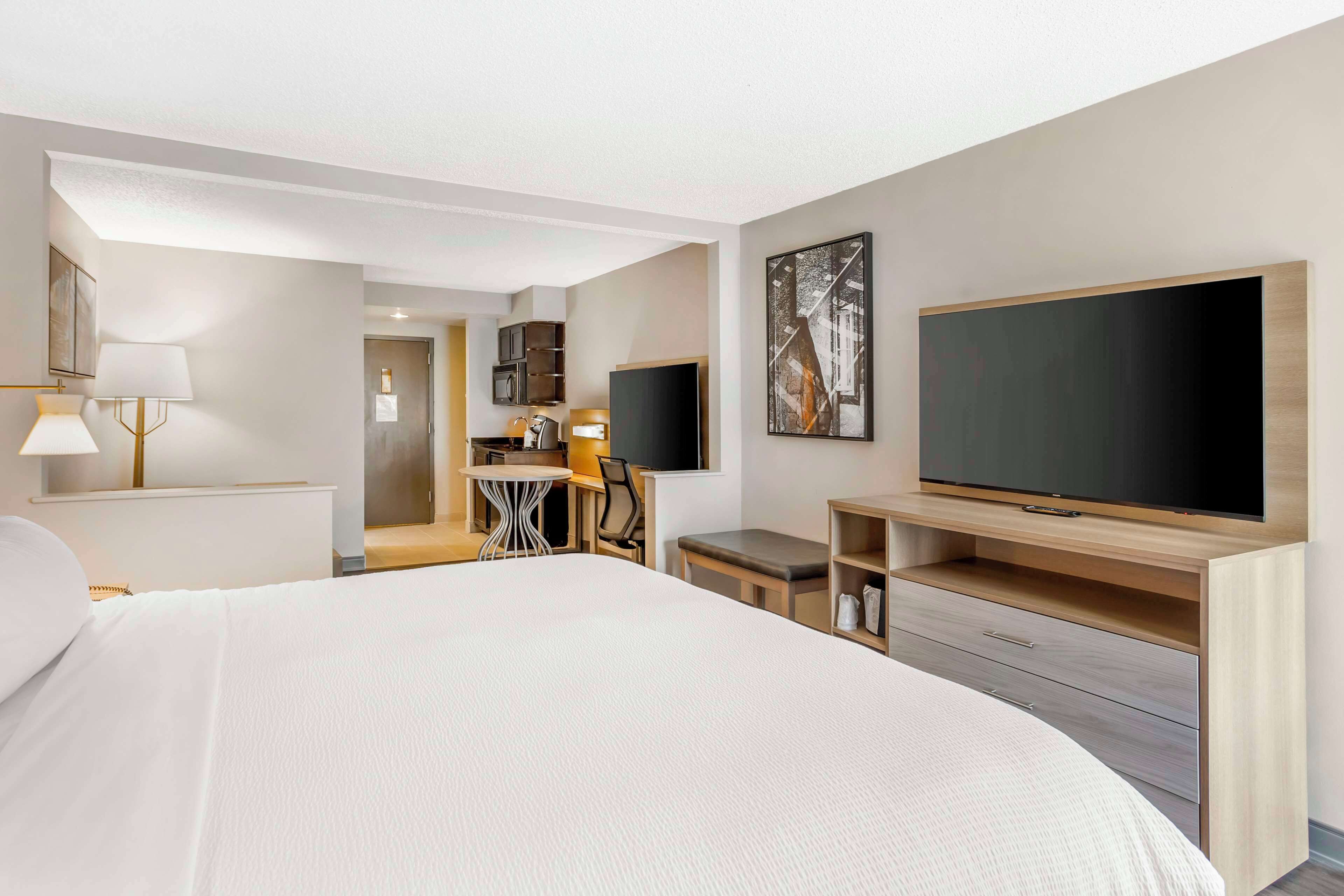 Habitación de hotel con una cama grande, televisión, escritorio con silla y una mesita.