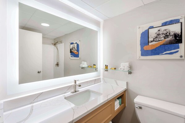 A modern bathroom with a large mirror, a marble sink, a toilet, and a shelf with toiletries. - Best Western Plus Heritage Rail-South York/I-83 (York)