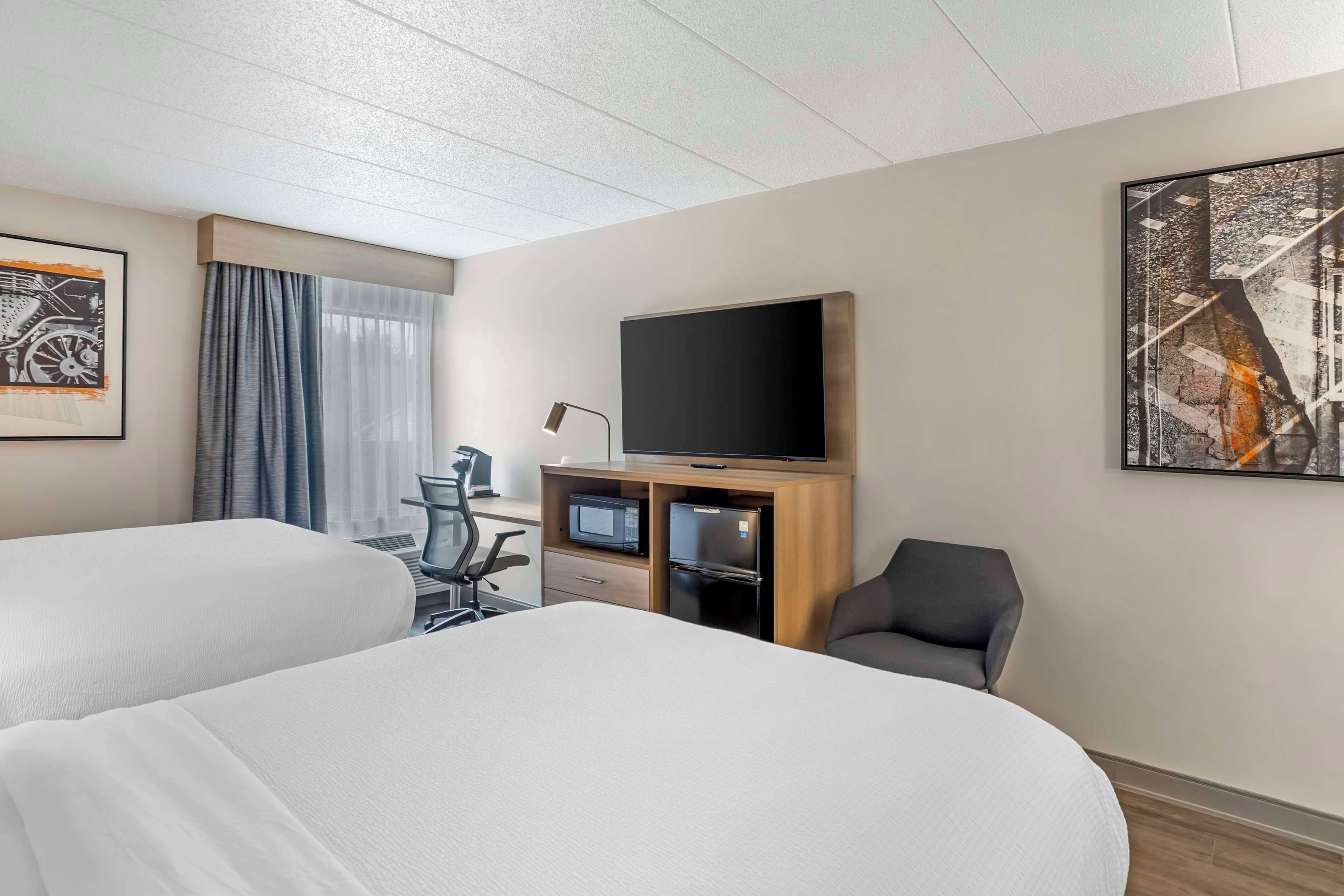 A hotel room with two beds, a desk with a computer, a flat-screen TV, and a chair.