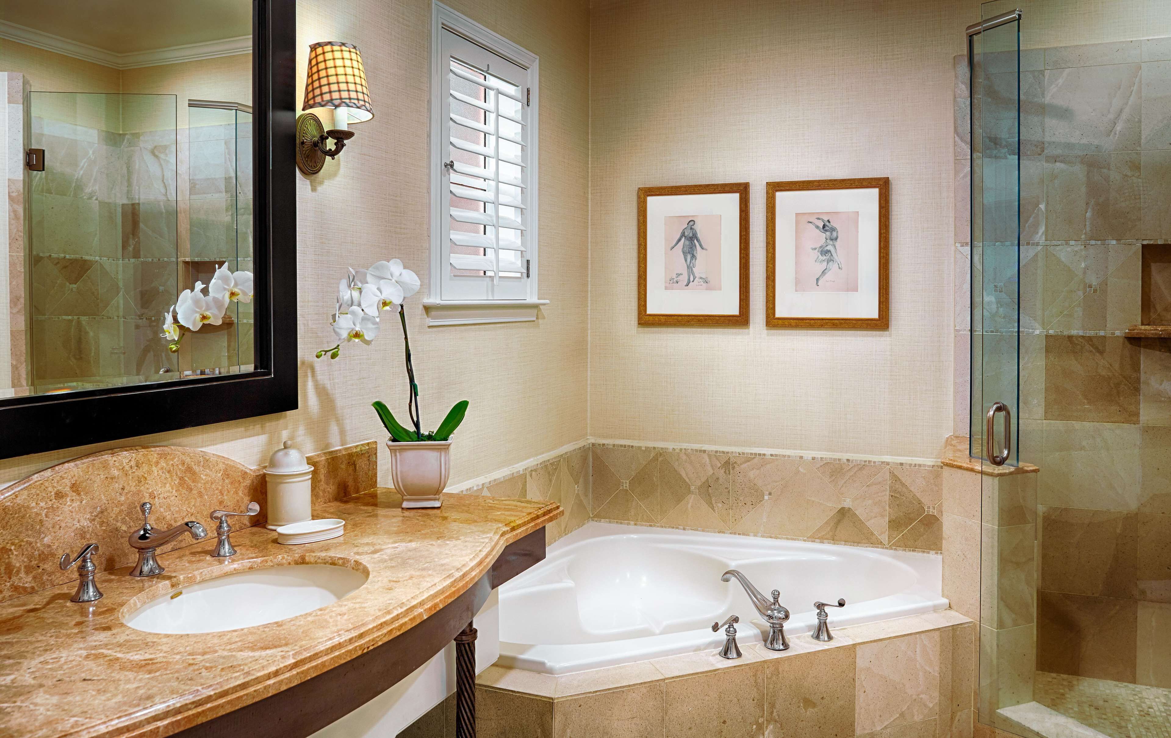 A bathroom with two sinks, a bathtub, a glass shower enclosure, a large mirror, and two framed pictures on the wall.
