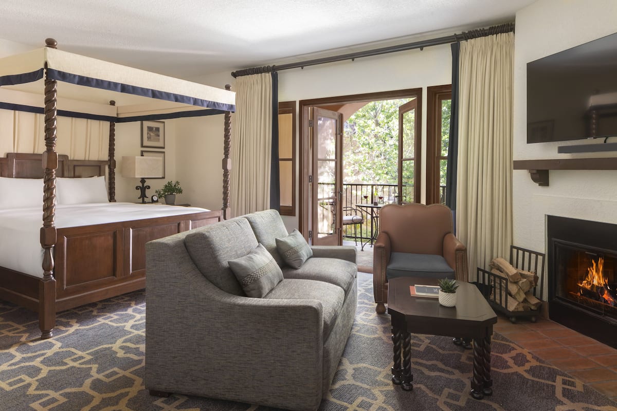 Un dormitorio con cama con dosel, un sofá gris, una silla, una mesita y una chimenea.