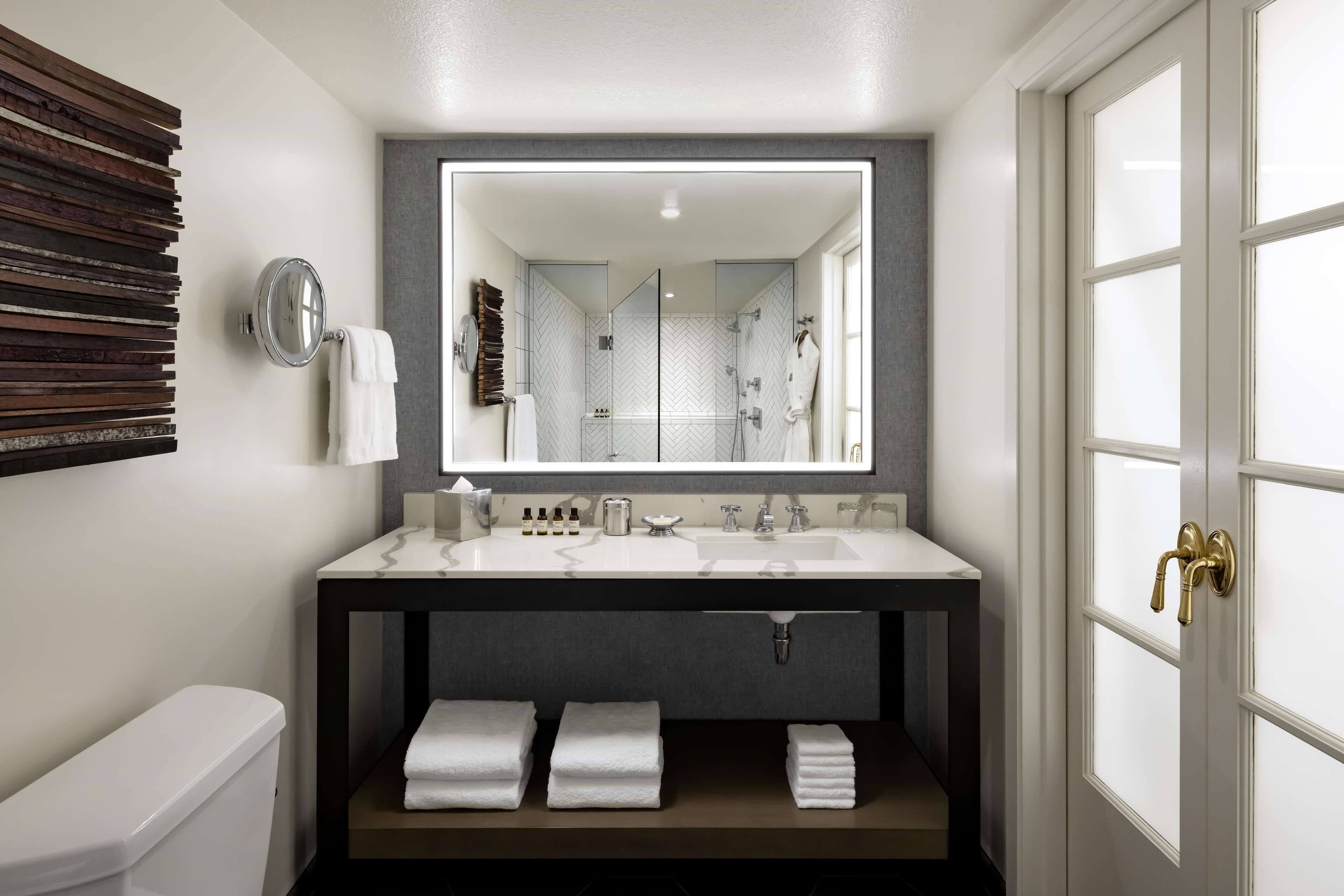 A modern bathroom with a large mirror, two sinks, and a toilet.