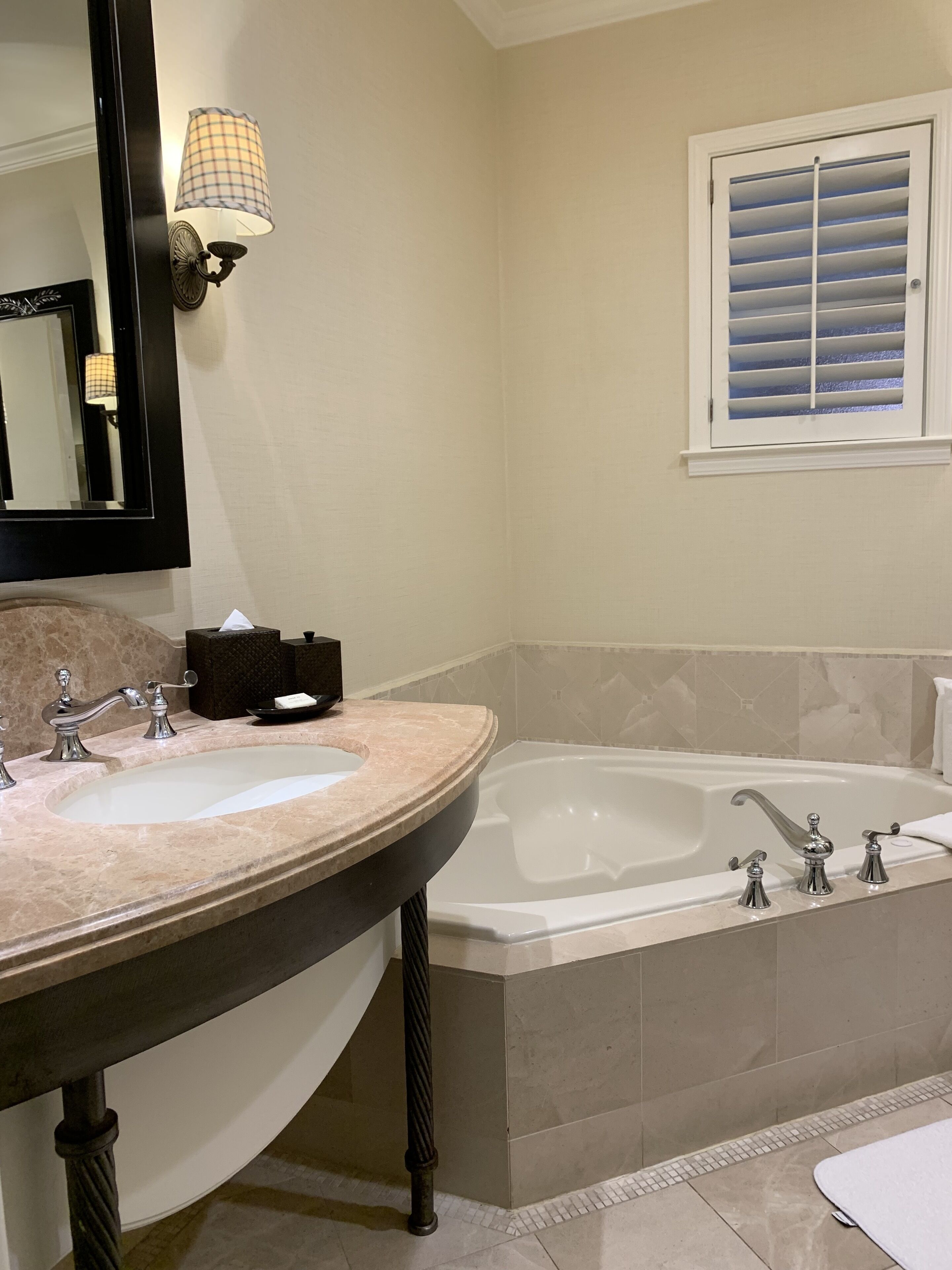 A bathroom with a large sink, a bathtub, and a window with blinds.