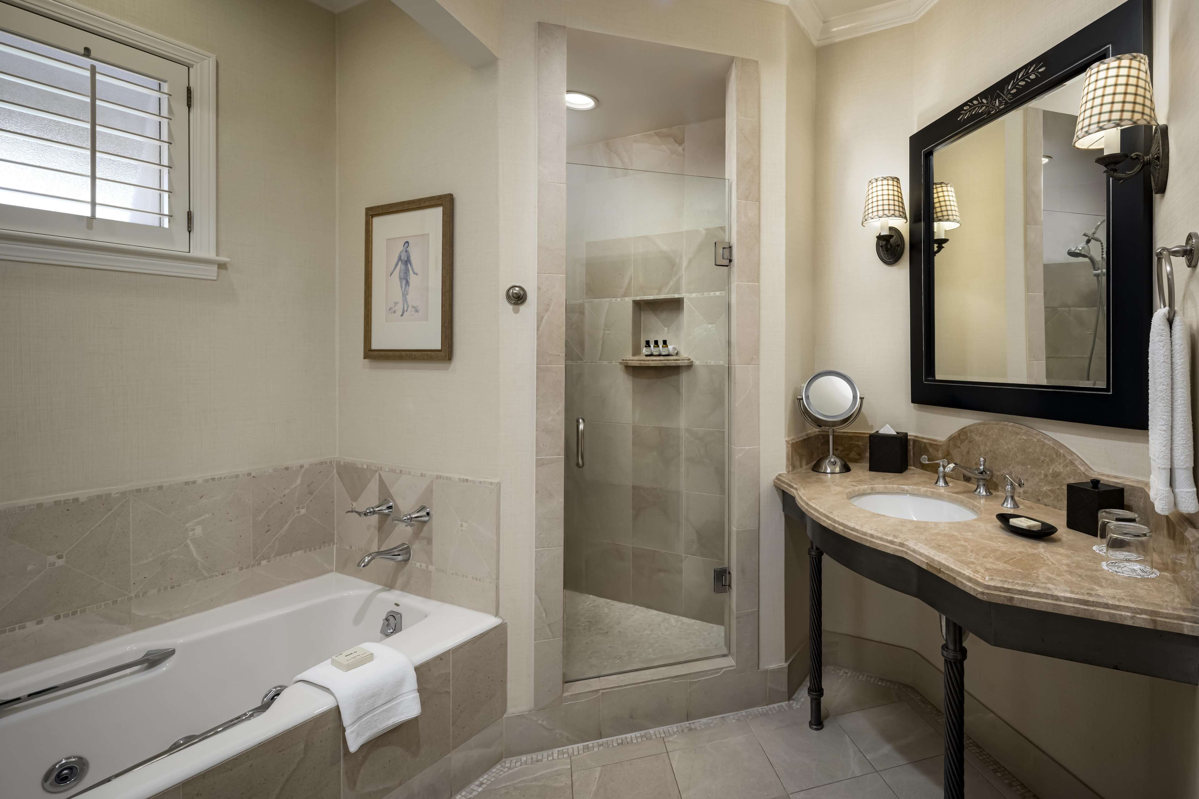 A modern bathroom with a bathtub, a glass-enclosed shower, a vanity with a mirror, and a framed picture on the wall.