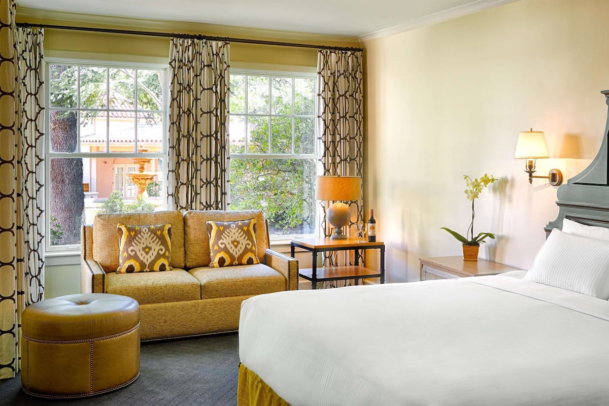 Habitación de hotel con una cama grande, un sofá, una mesita con lámpara y vistas al exterior.