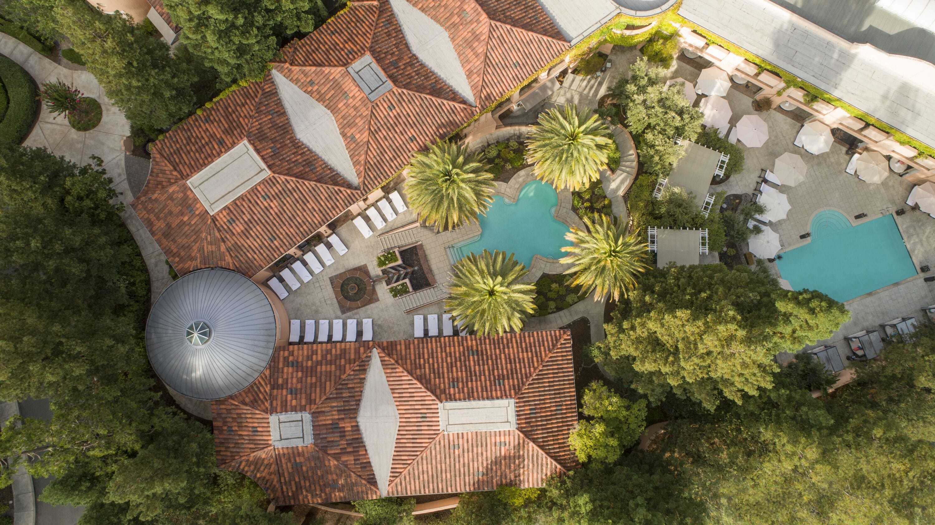 Vista aérea de un resort con piscina, palmeras y una gran estructura en forma de cúpula.
