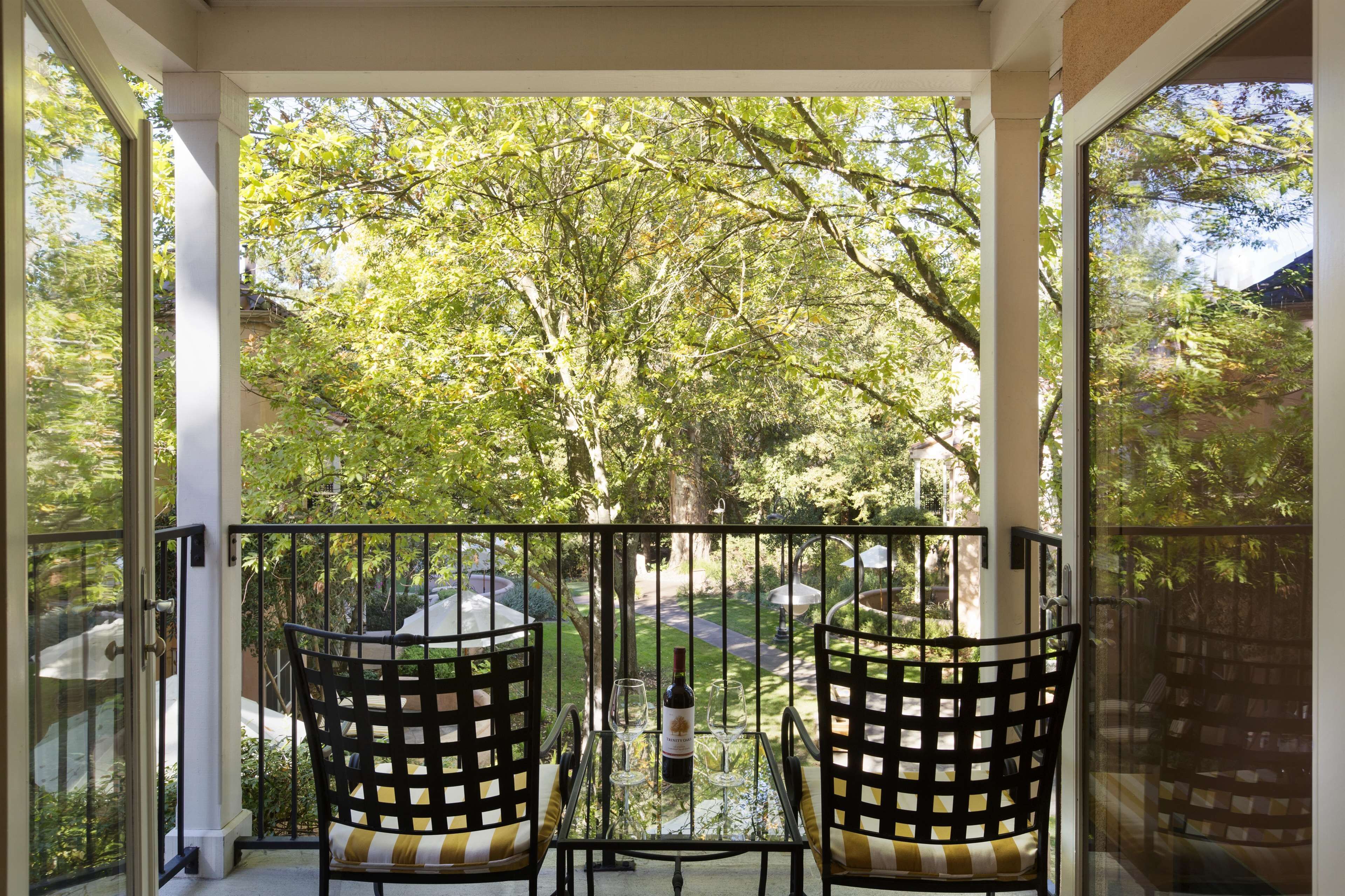 Un balcon avec deux chaises et une table, donnant sur un jardin avec des arbres et un sentier.