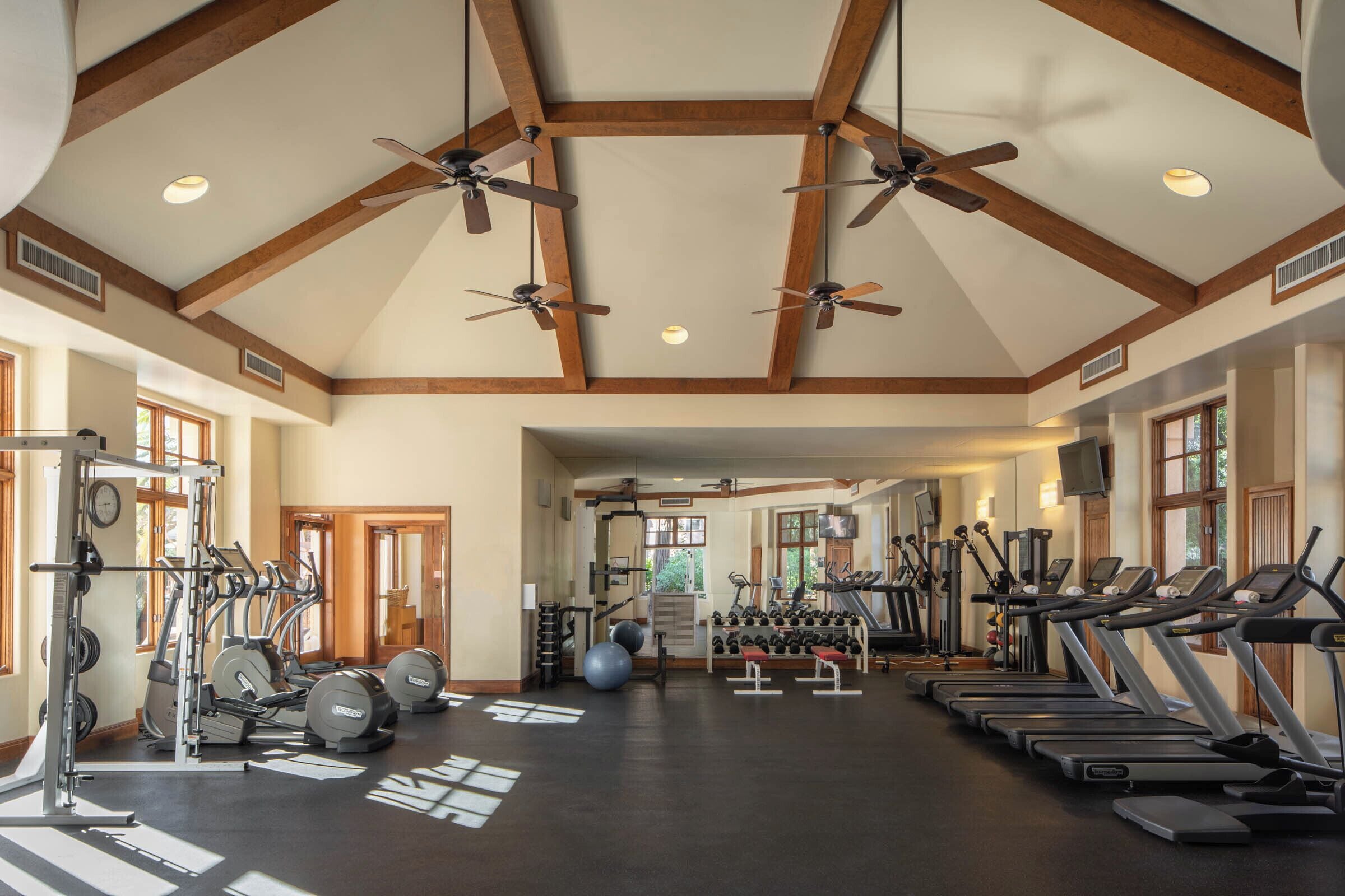 A spacious gym with ceiling fans, treadmills, and various exercise equipment.
