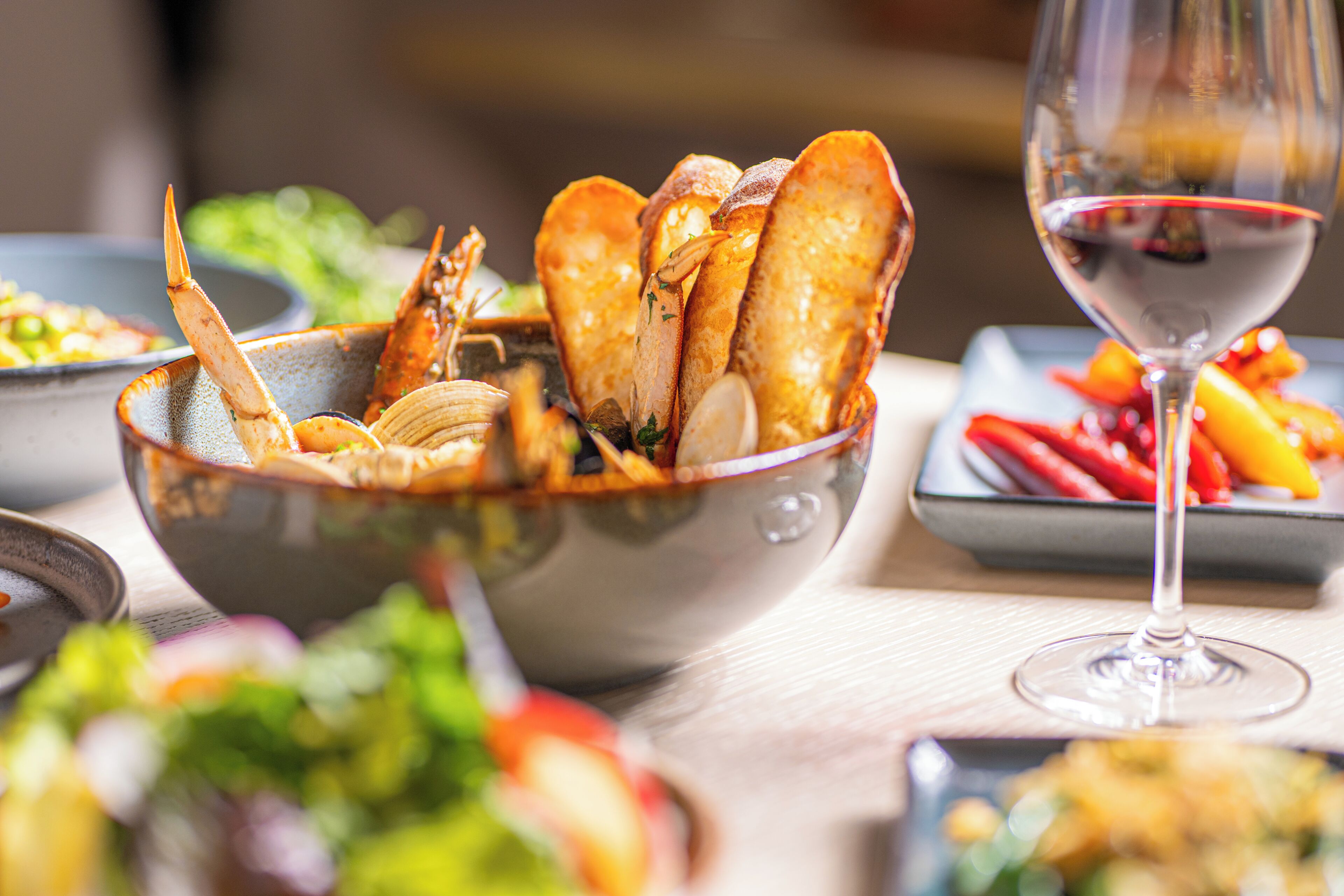 A dining table with a bowl of seafood, a glass of red wine, and various dishes.