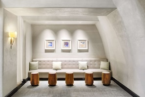 A modern interior with a beige sofa, three wooden stools, and wall-mounted picture frames.