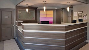 Un comptoir d’accueil au design moderne, un grand miroir au-dessus, et un mur orné de panneaux d’information encadrés.