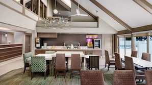 Une salle à manger d’hôtel avec un plafond haut, un lustre moderne et une vue sur la cuisine en arrière-plan.
