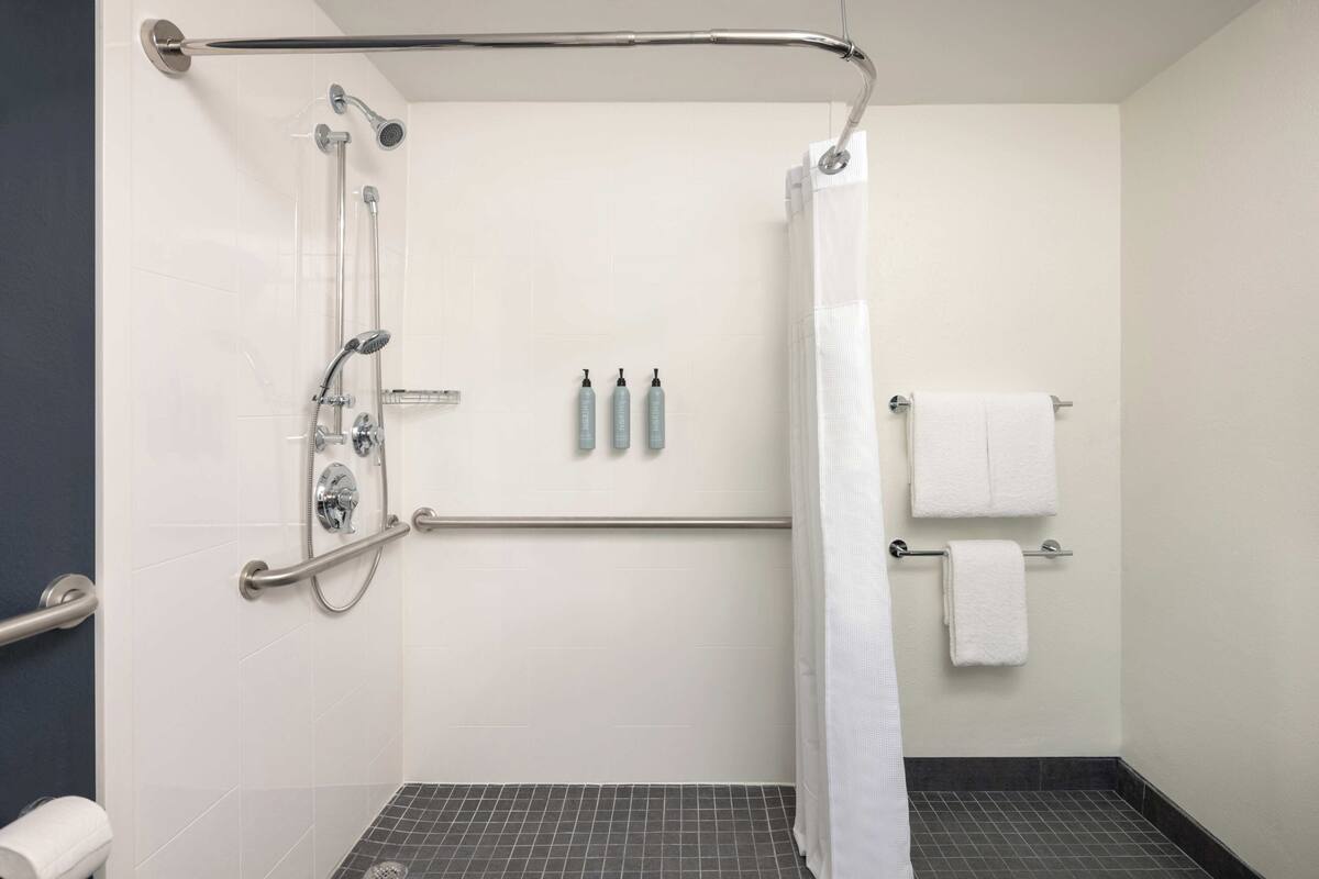 A modern bathroom with a shower, grab bars, a towel rack, and a toilet.