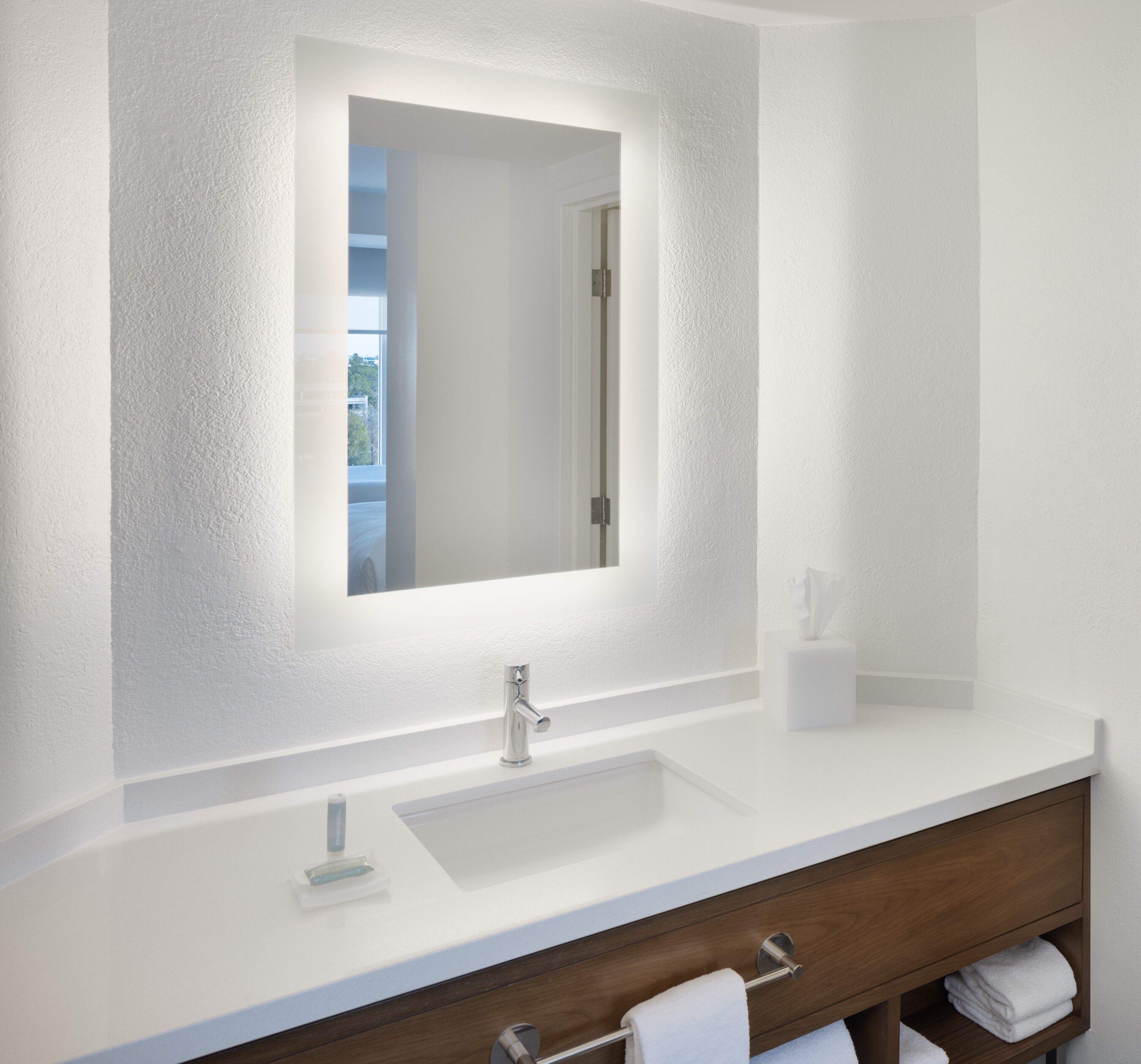 Une salle de bain moderne avec un meuble-lavabo blanc, un grand miroir et une porte visible donnant sur une autre pièce.