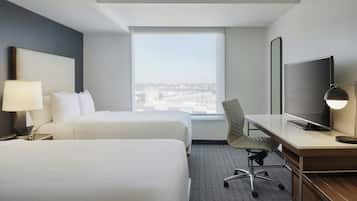 Une chambre d’hôtel avec deux lits, un bureau, une chaise, une télévision et une grande fenêtre donnant sur la ville.