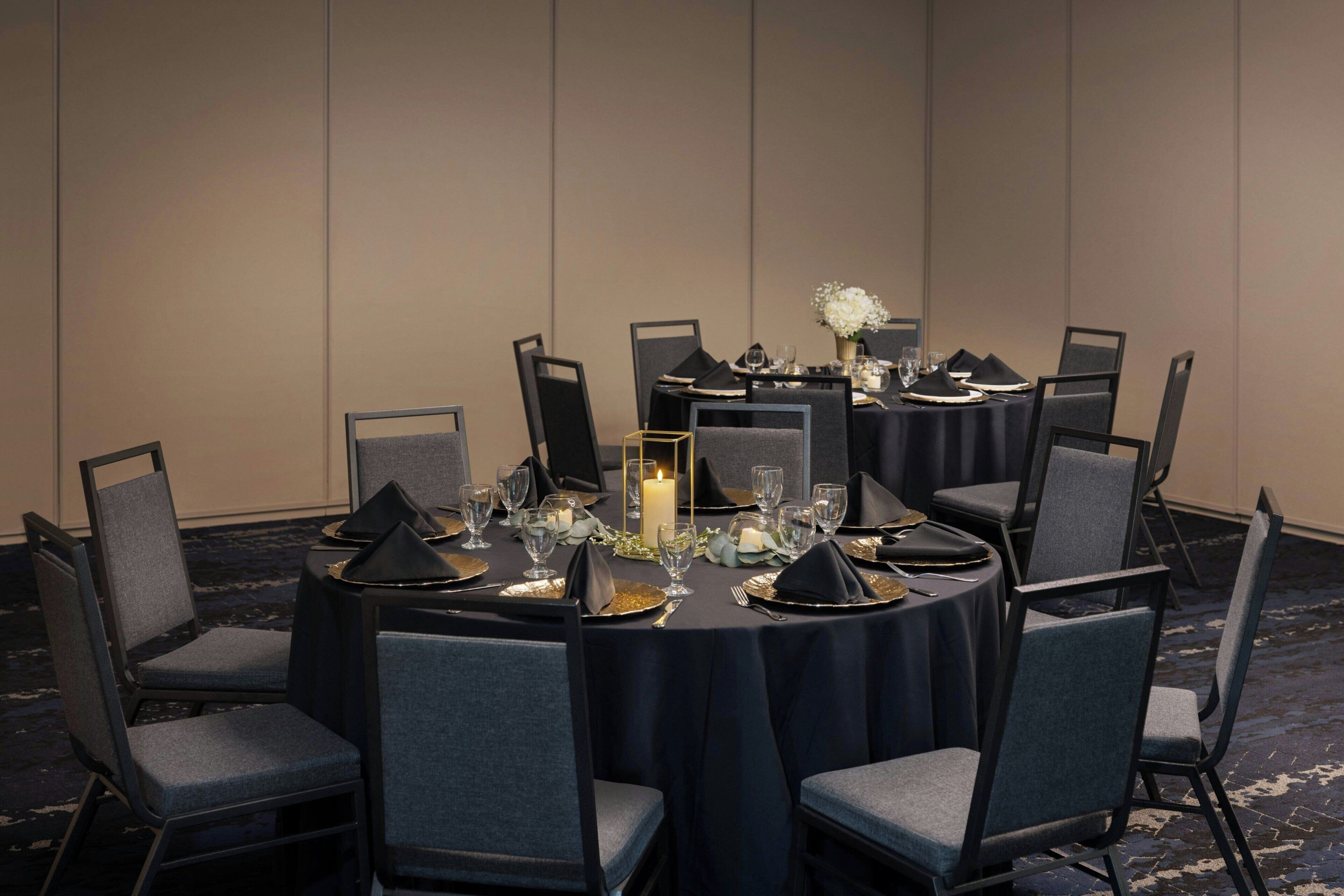A conference room with round tables, grey upholstered chairs, and a dark tablecloth.