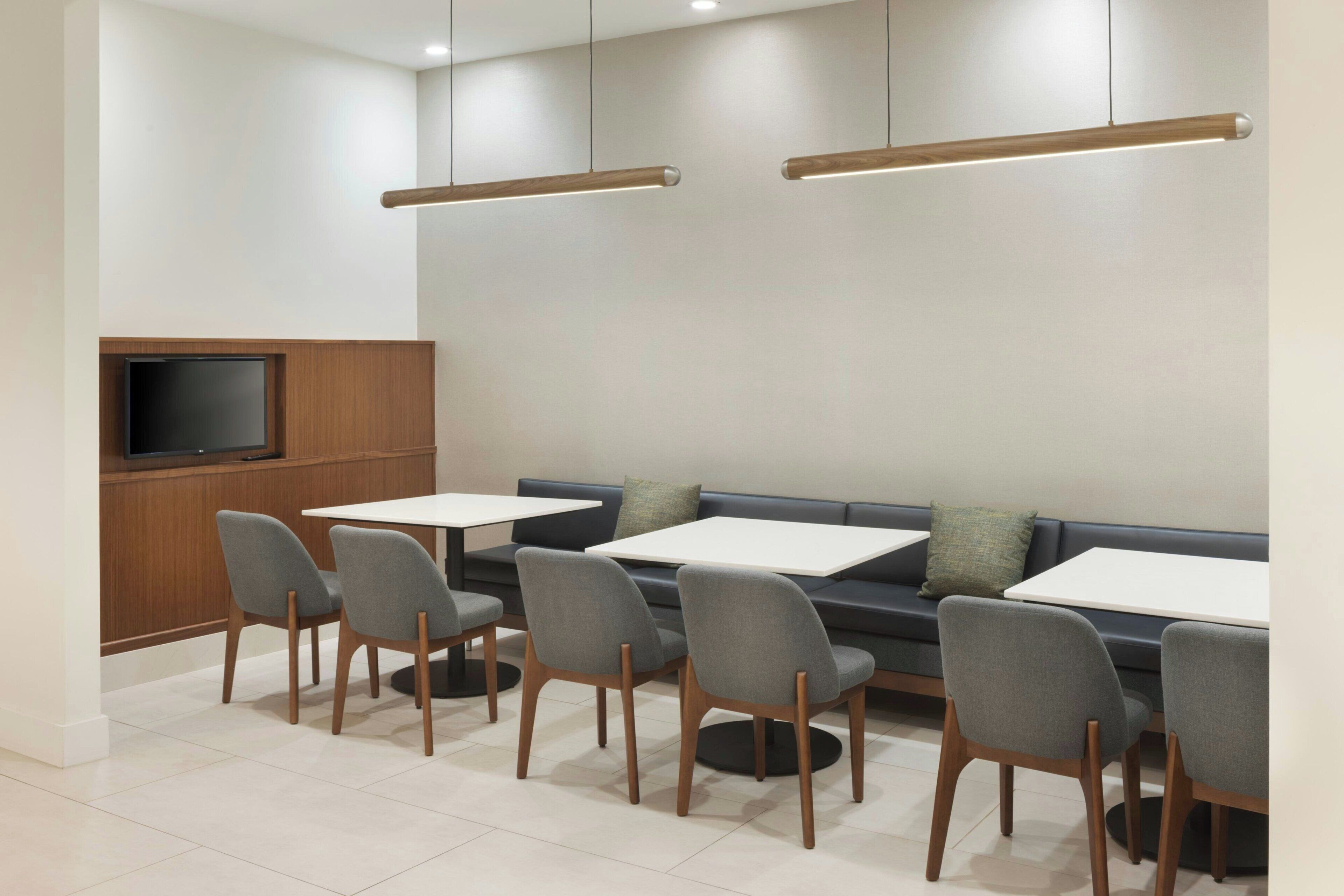 A modern dining area with a flat-screen TV, grey upholstered chairs, and a dark-colored sofa.