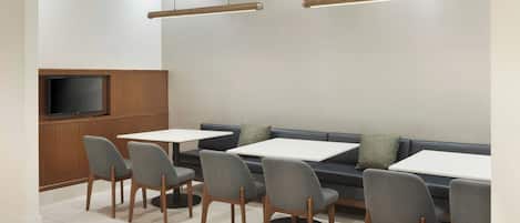 A modern dining area with a flat-screen TV, grey upholstered chairs, and a dark-colored sofa.
