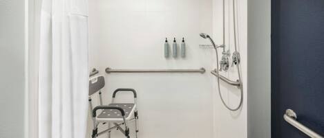 A shower area with a grab bar, a wheelchair, and two bottles of shampoo.