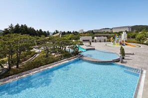 A swimming pool with a slide, surrounded by trees and a building in the background.