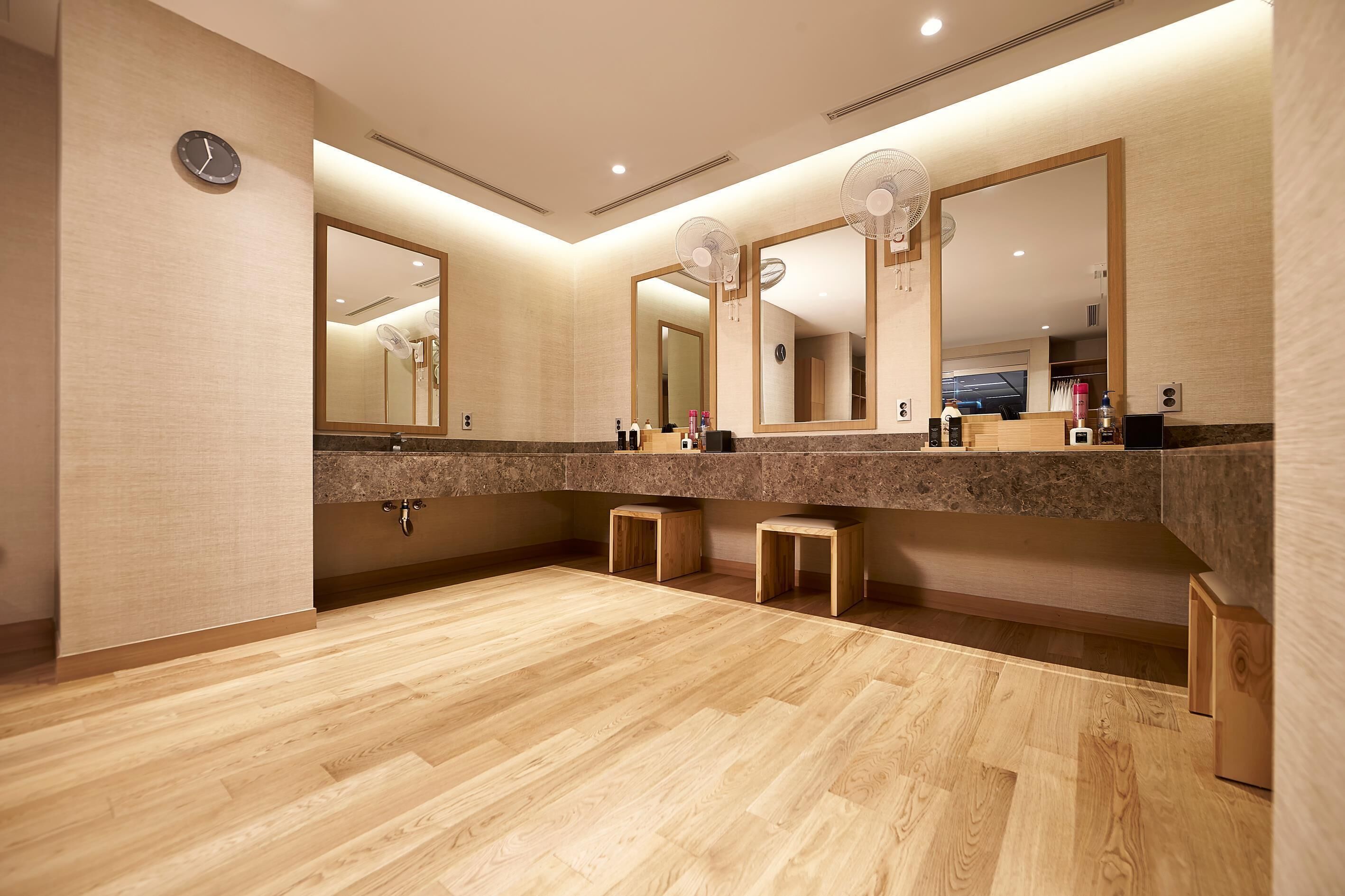 A modern bathroom with a wooden floor, a large mirror, and a clock on the wall.