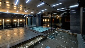Un área de piscina interior moderna con pared de vidrio, zona de estar e iluminación adecuada.