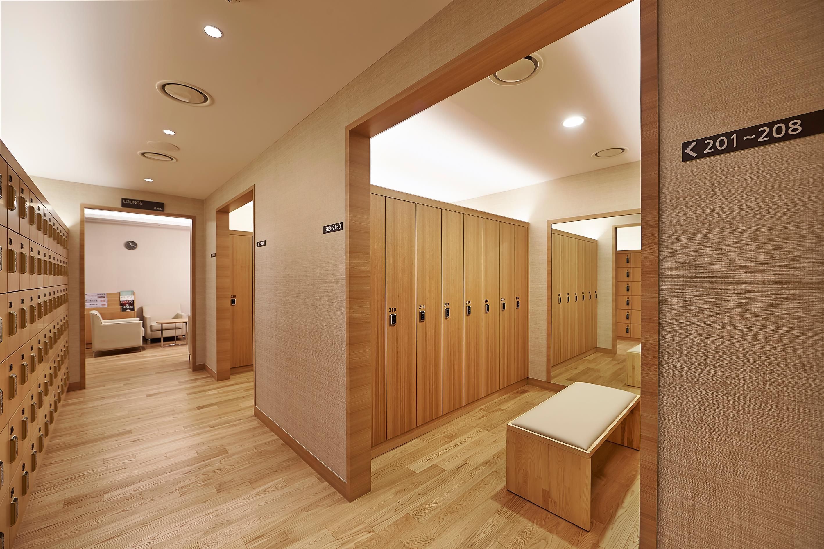 A hotel corridor with lockers, a seating area, and wooden lockers numbered 201-208.