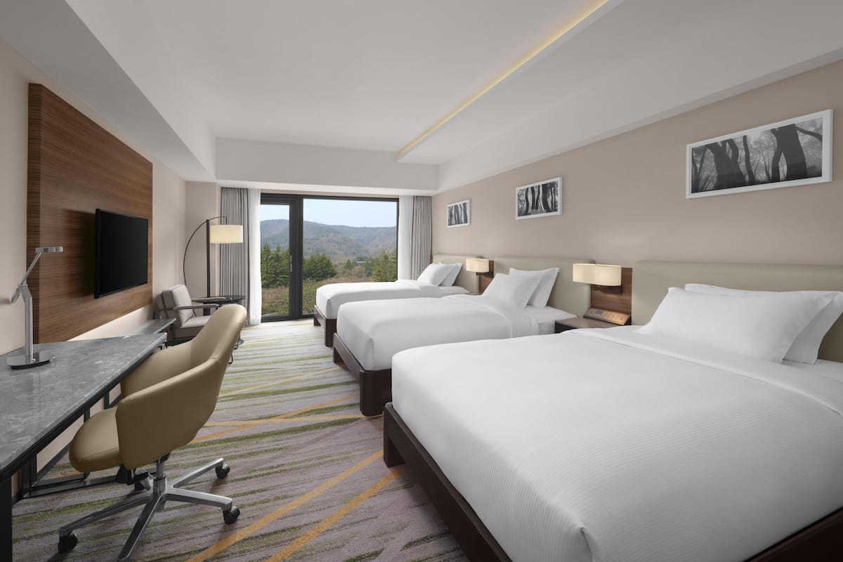 A hotel room with two beds, a desk, a chair, a TV, and a view of the mountains.