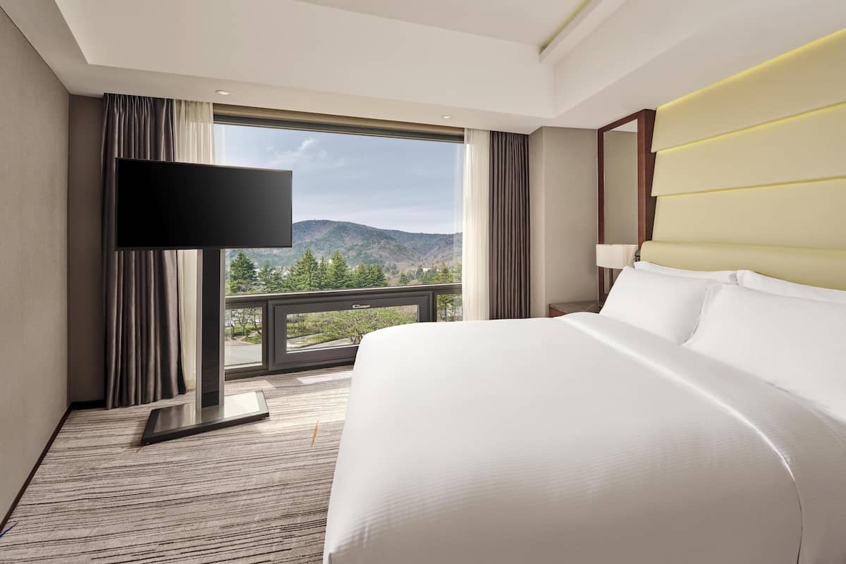 A hotel room with a large bed, a flat-screen TV, a view of mountains, and a balcony.