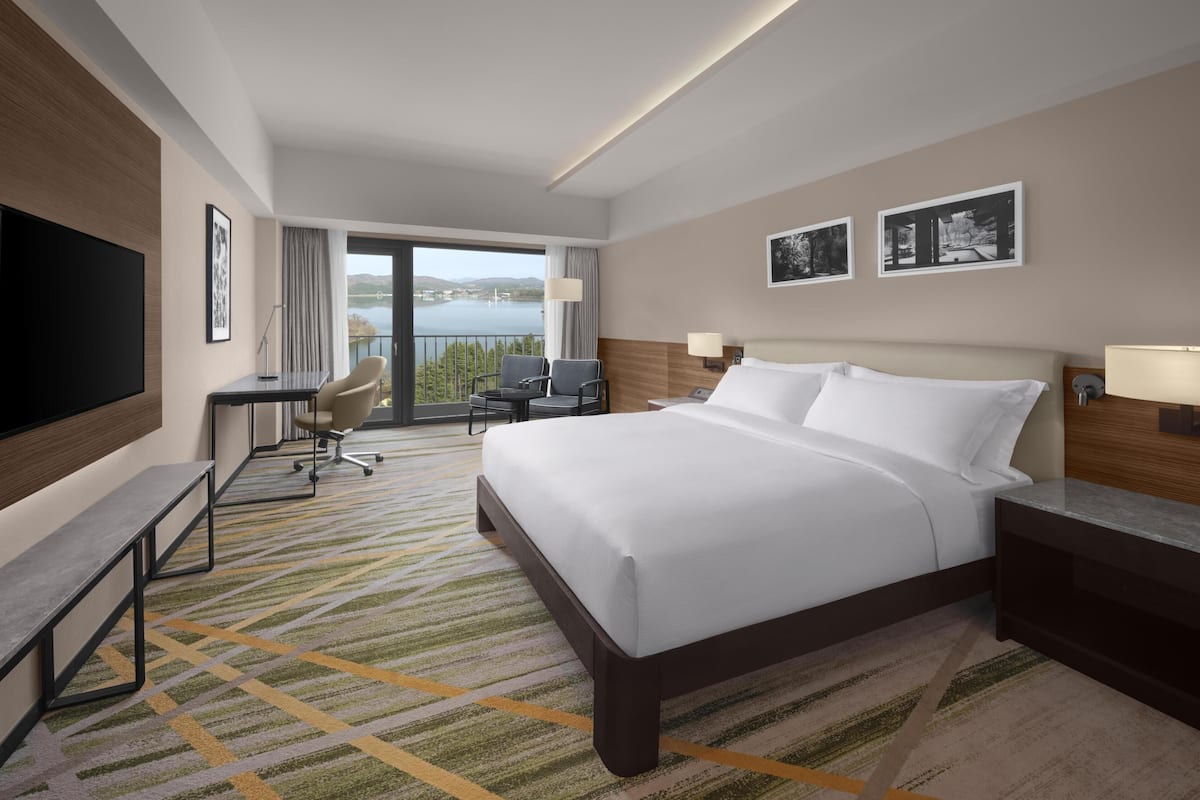 A hotel room with a bed, desk, chairs, and a TV.