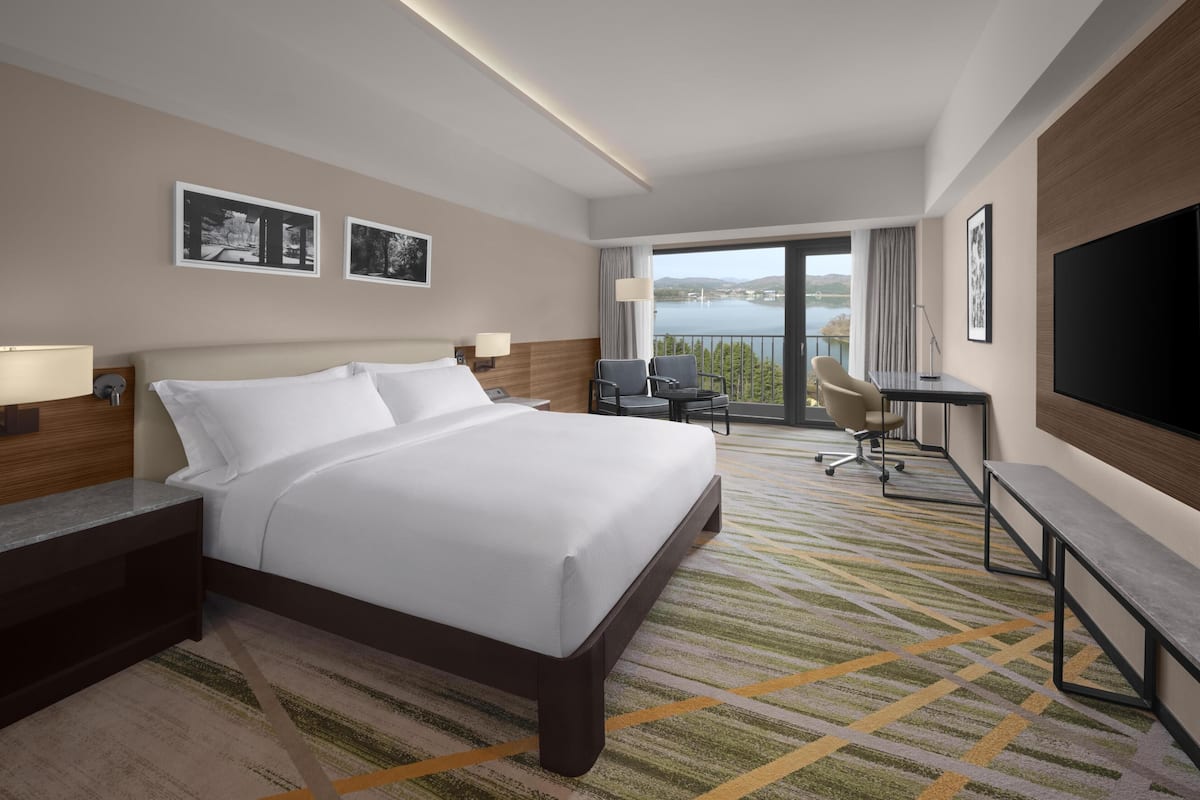 A hotel room with a large bed, a desk, a chair, a TV, and a view of the outdoors.