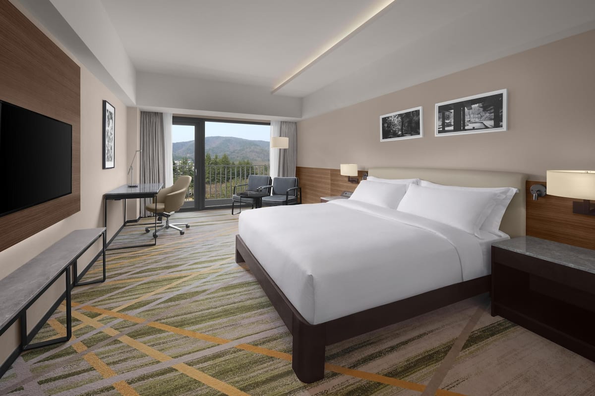 A hotel room with a large bed, a desk, a chair, and a TV.