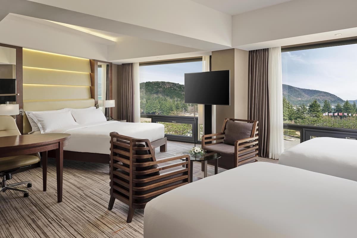 A hotel room with a large bed, a desk, a chair, a TV, and a view of mountains.