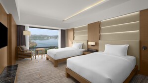 Habitación de hotel con dos camas, televisión, una mesita y vista a un lago.