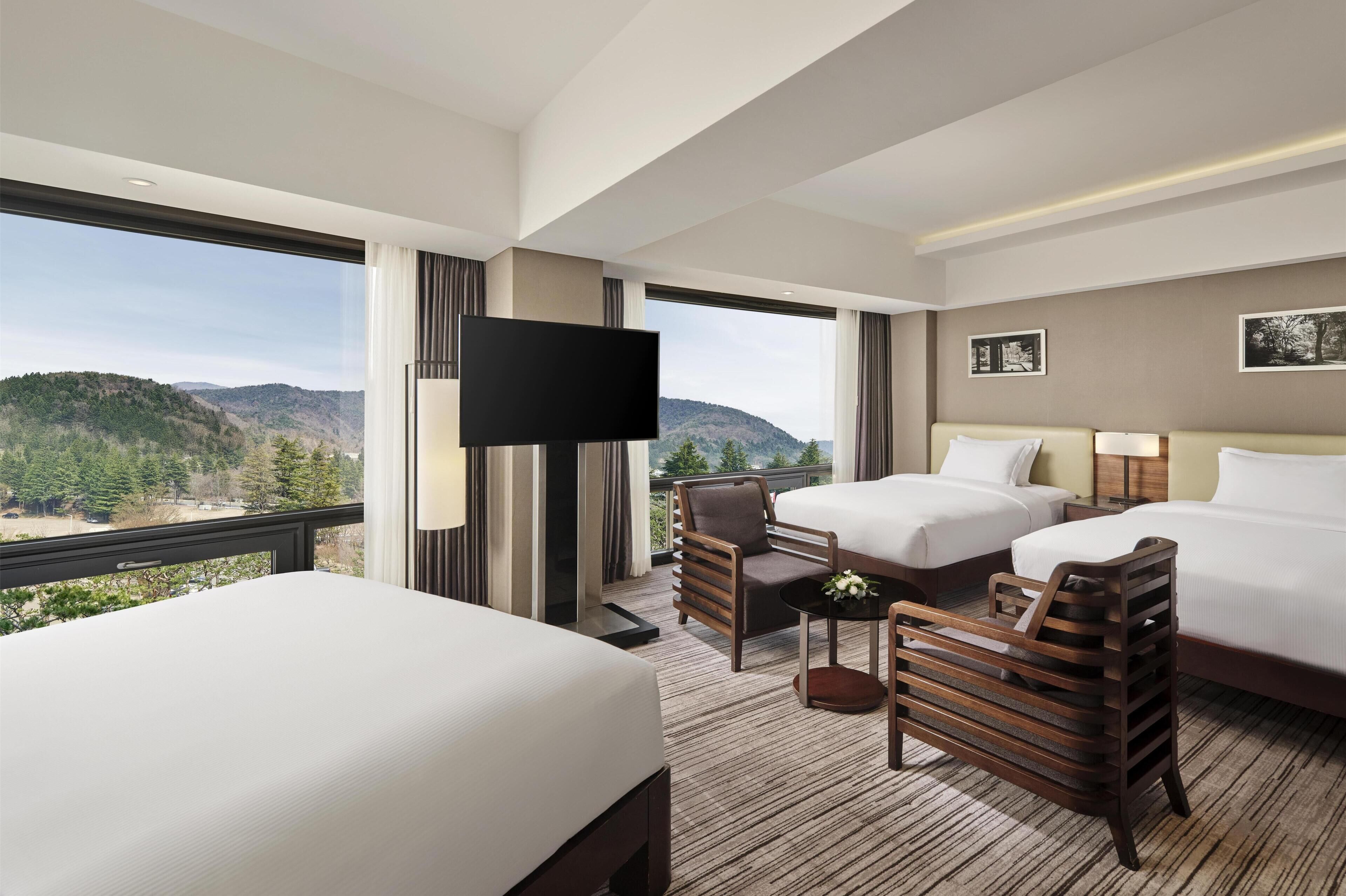 Ein Hotelzimmer mit zwei Betten, einem Fernseher, einem Schreibtisch und Bergblick.