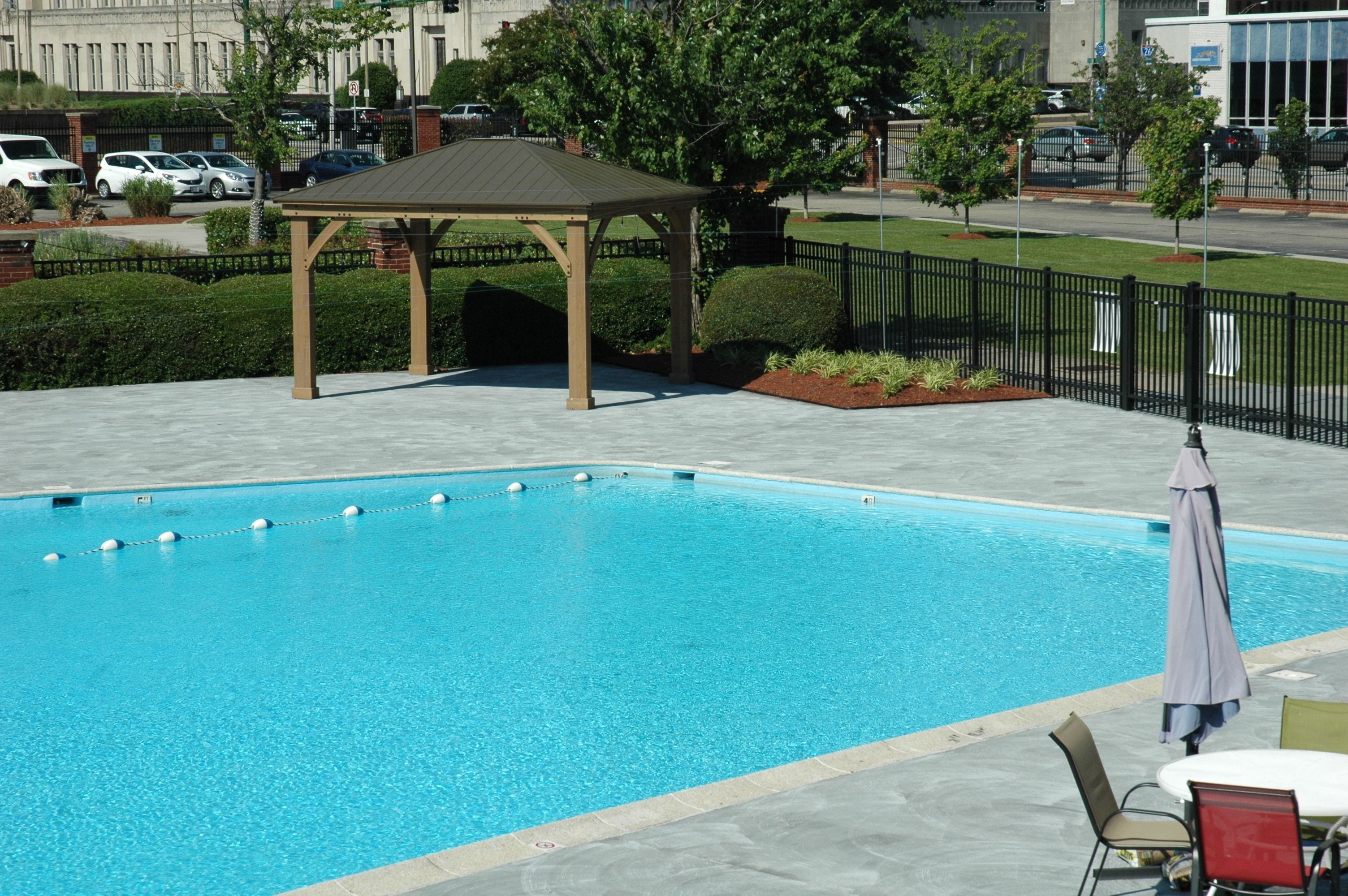 A rectangular swimming pool with a wooden gazebo and a fenced area with benches.